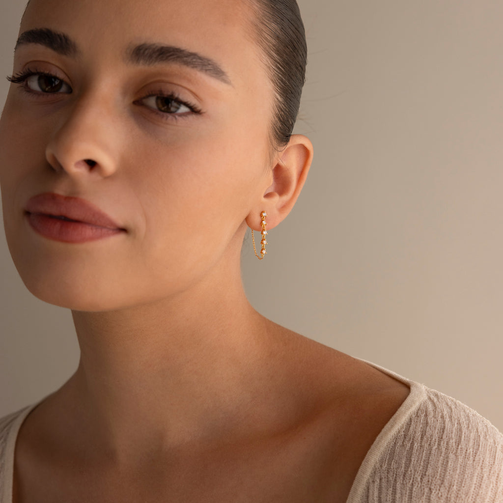 A woman with tied-back hair and a cream top wears Diamond Chain Drop Earrings, gazing softly at the camera against a neutral background.