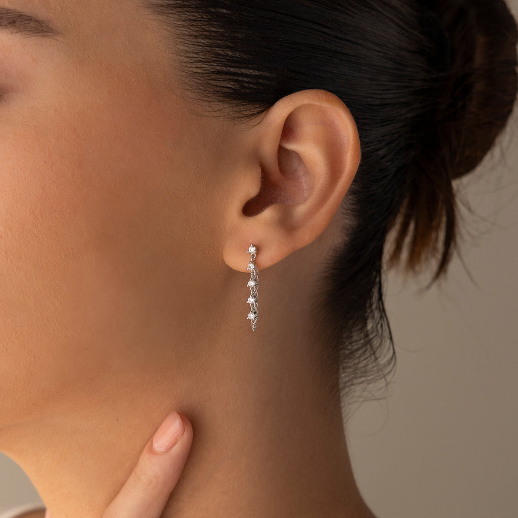 Close-up of a womans ear wearing Diamond Chain Drop Earrings in Silver, featuring multiple small stones, with her hand resting near her chin.