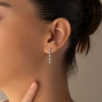 Close-up of a womans ear wearing Diamond Chain Drop Earrings in Silver, featuring multiple small stones, with her hand resting near her chin.