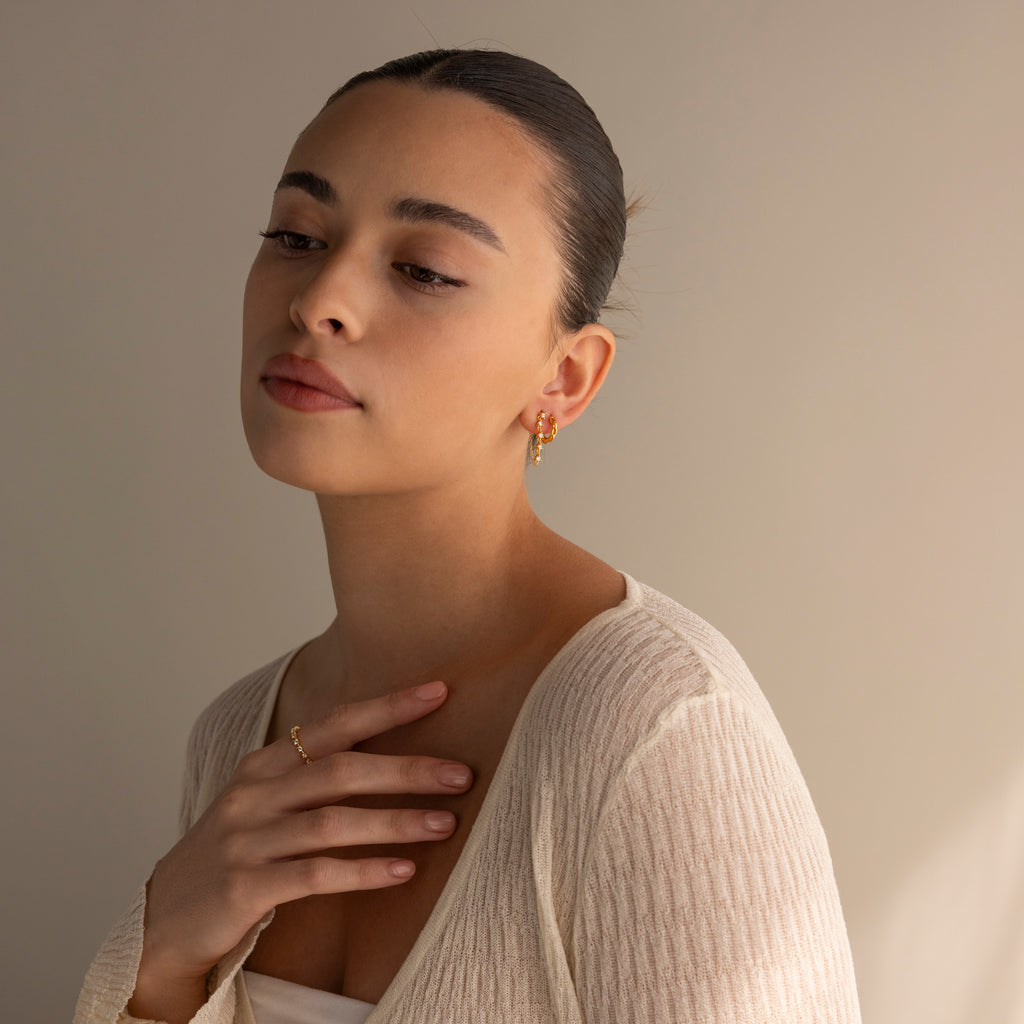 A woman with slicked-back hair and a cream textured top gazes downward thoughtfully, showcasing elegant Diamond Chain Drop Earrings.