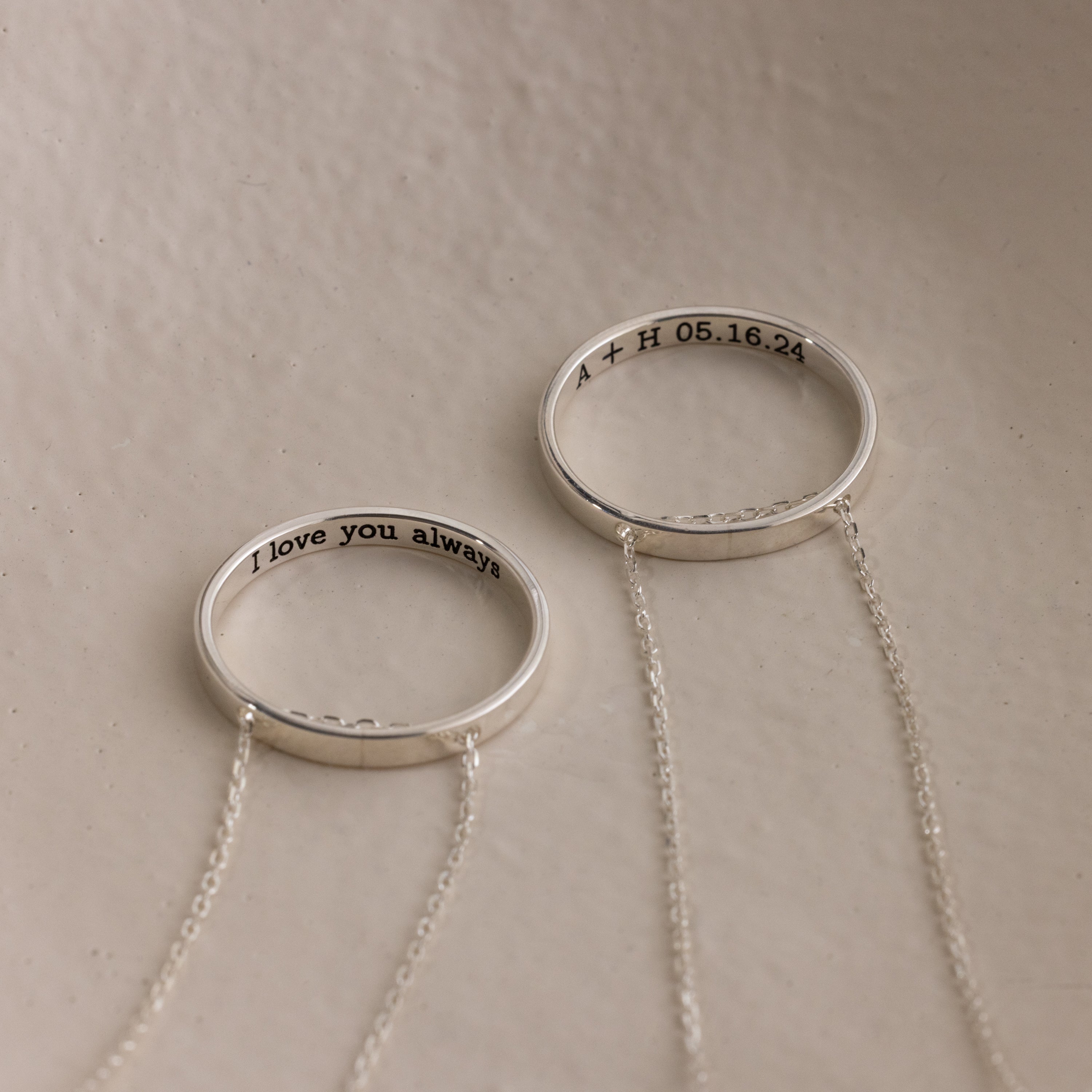 The Inner Circle Necklace features two silver rings with chains: one engraved "I love you always," the other with "A + H 05.16.24" inside, creating a modern amulet style.