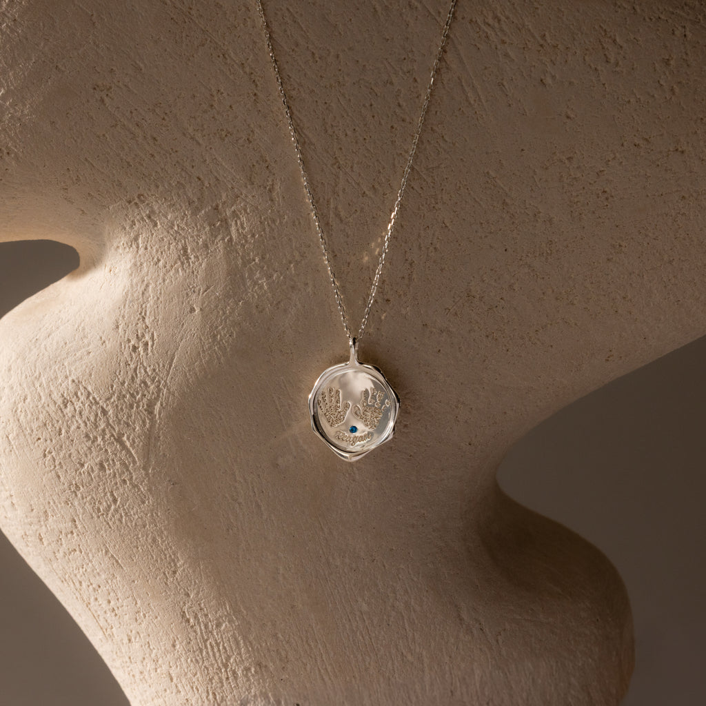 The Baby Hand & Footprint Necklace in Sterling Silver, displayed on a mannequin, is a personalized keepsake for honoring special moments and cherishing memories close to your heart.