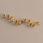 Floating Birthstone Huggies—gold hoops with vibrant gemstones—are arranged diagonally on a beige surface, ideal for fans of personalized jewelry.