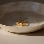 The Moonstone Cluster Ring with three round stones rests in a textured, cream-colored dish under soft lighting.