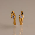 The Floating Diamond Huggies are twisted gold hoop earrings with a modern design, each featuring a single round diamond—an elegant addition to your personalized jewelry collection.