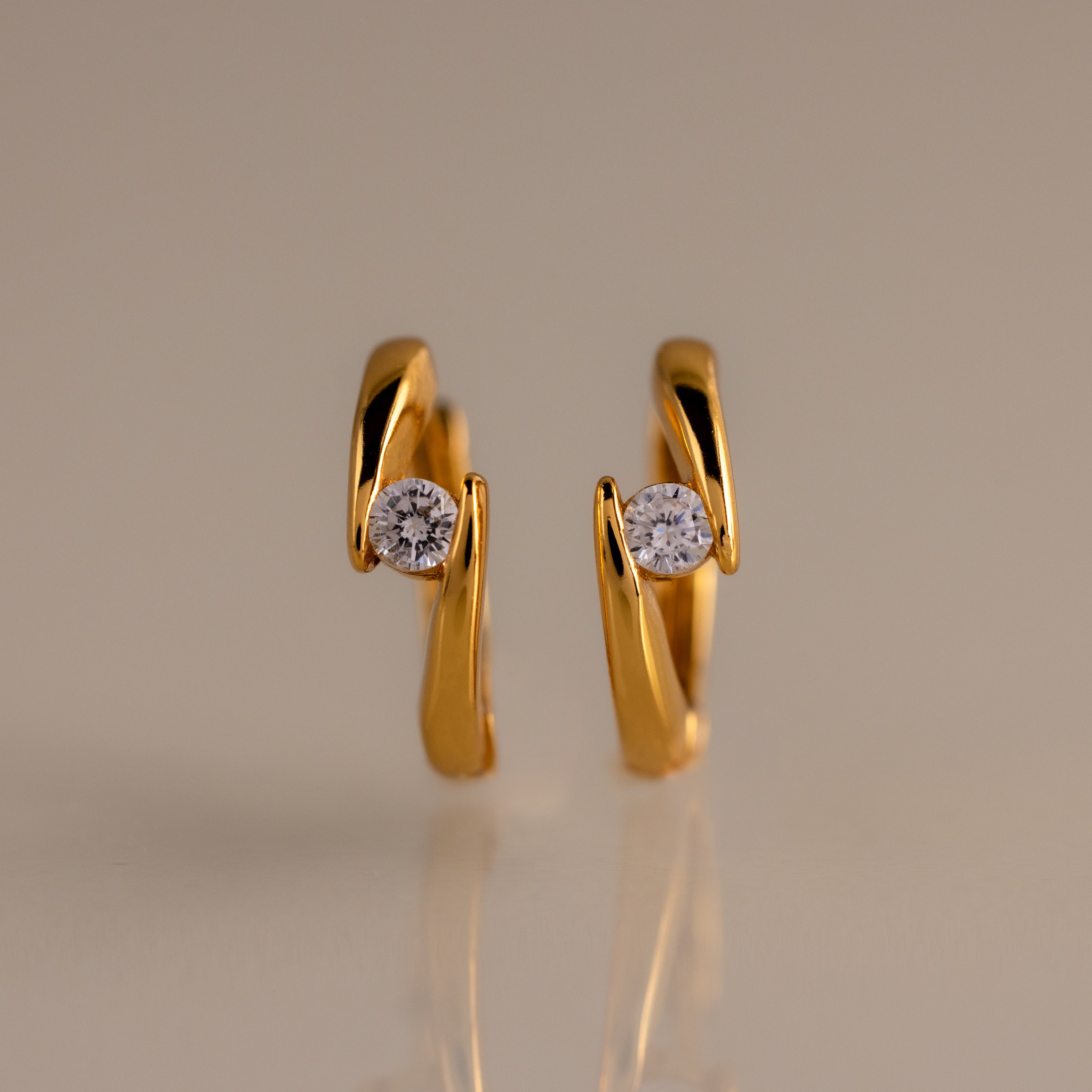 The Floating Diamond Huggies are twisted gold hoop earrings with a modern design, each featuring a single round diamond—an elegant addition to your personalized jewelry collection.