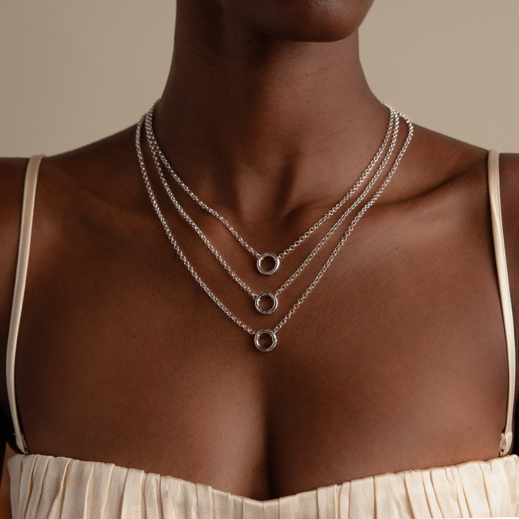 A woman wears a cream top and a Rolo Circle Charm Necklace in Sterling Silver featuring three layered circular pendants.