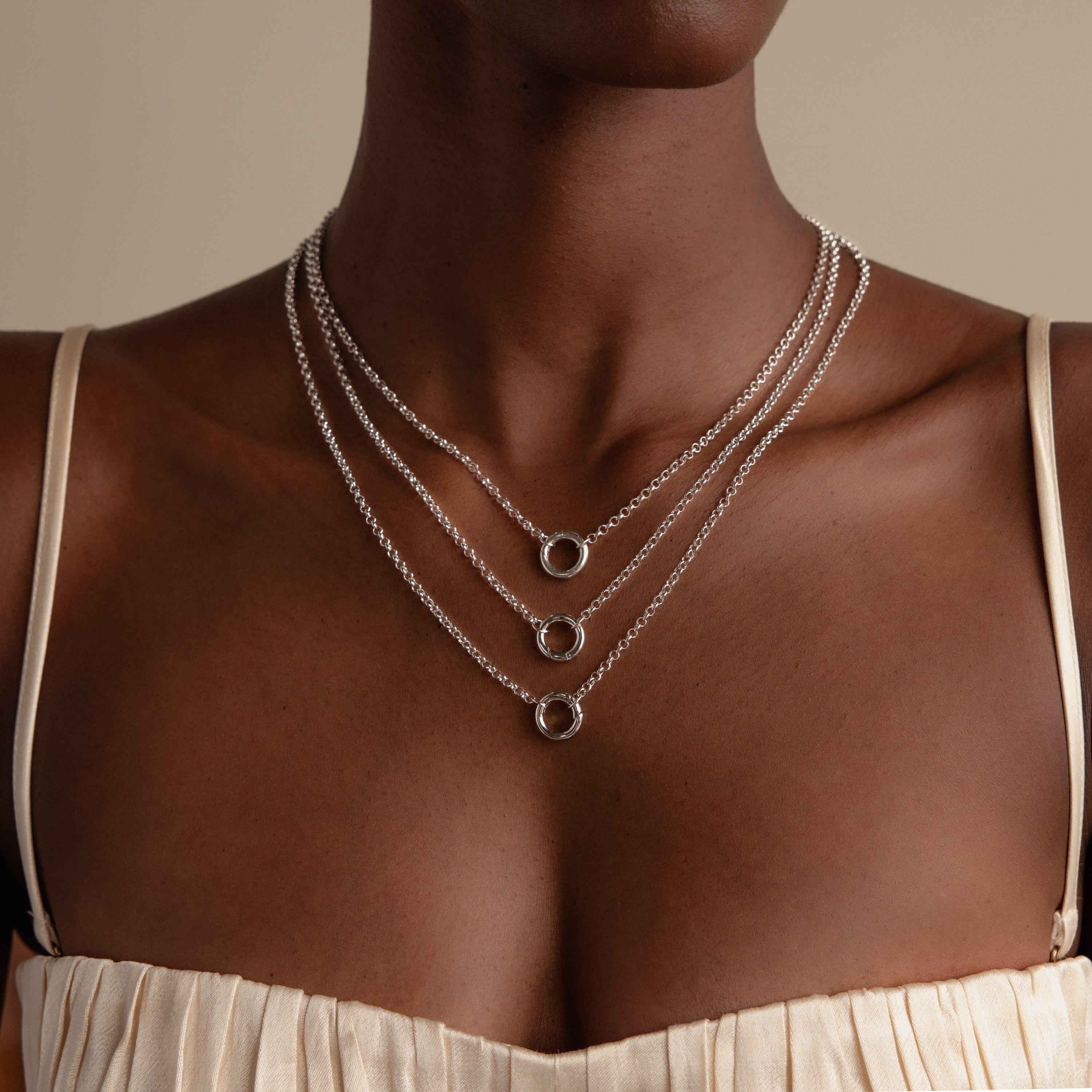 A woman wears a cream top and a Rolo Circle Charm Necklace in Sterling Silver featuring three layered circular pendants.