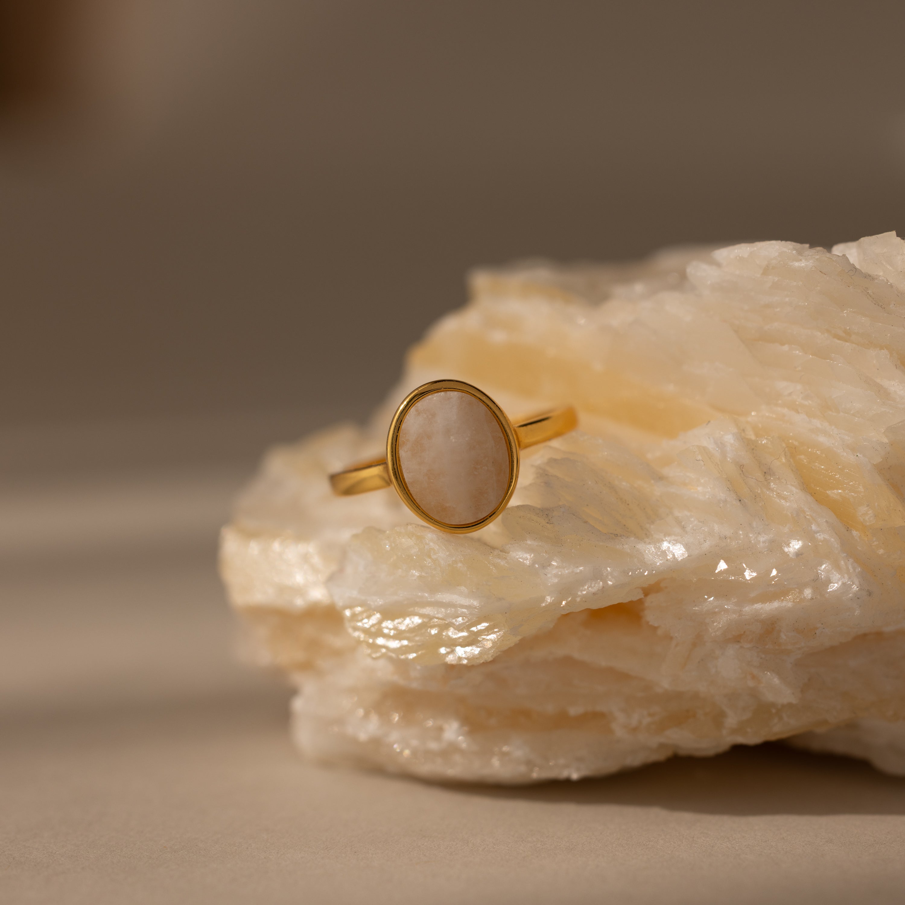 The Moonstone Signet Ring, featuring an oval white stone, is displayed on a textured cream rock—an elegant piece of everyday jewelry.