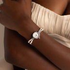 A woman wearing the Beaded Pearl Timepiece in Sterling Silver on her wrist, styled with a cream-colored pleated dress.