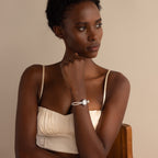 A woman in a cream top sits on a chair, thoughtfully gazing to the side while wearing the Beaded Pearl Timepiece in Sterling Silver.