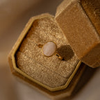 The Moonstone Signet Ring showcases an oval white moonstone on a gold minimalist band, elegantly displayed in an open textured beige velvet box—a perfect choice for everyday jewelry style.
