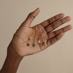 A hand holds five North Star Gemstone Necklaces in 18K Gold, each with a small rectangular crystal pendant, displayed on a beige background.