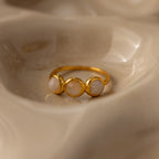 The Moonstone Cluster Ring, featuring three round pale moonstones, rests on a smooth beige surface—an elegant example of modern jewelry.