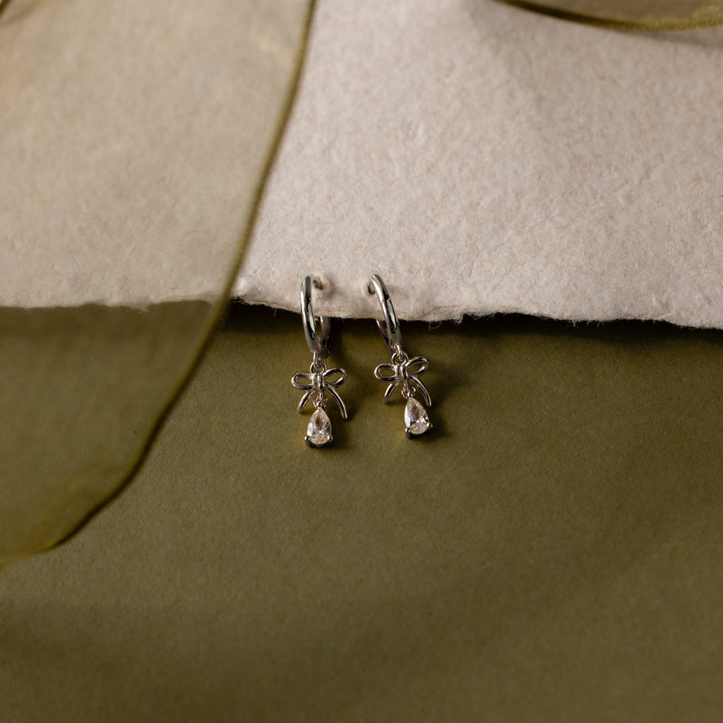 Flatlay of our Teardrop Ribbon Charm Hoops in Silver against a white and green background