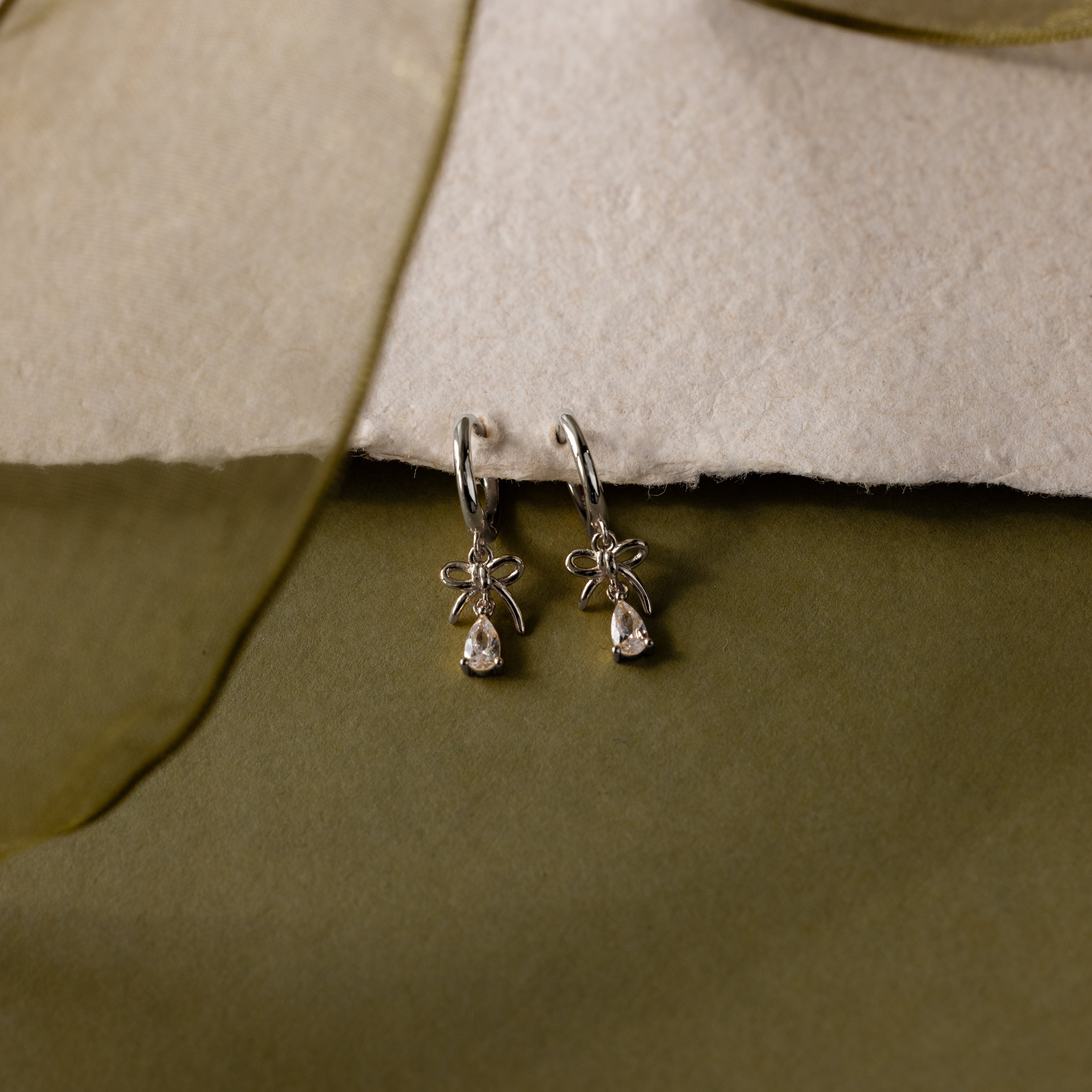 Flatlay of our Teardrop Ribbon Charm Hoops in Silver against a white and green background