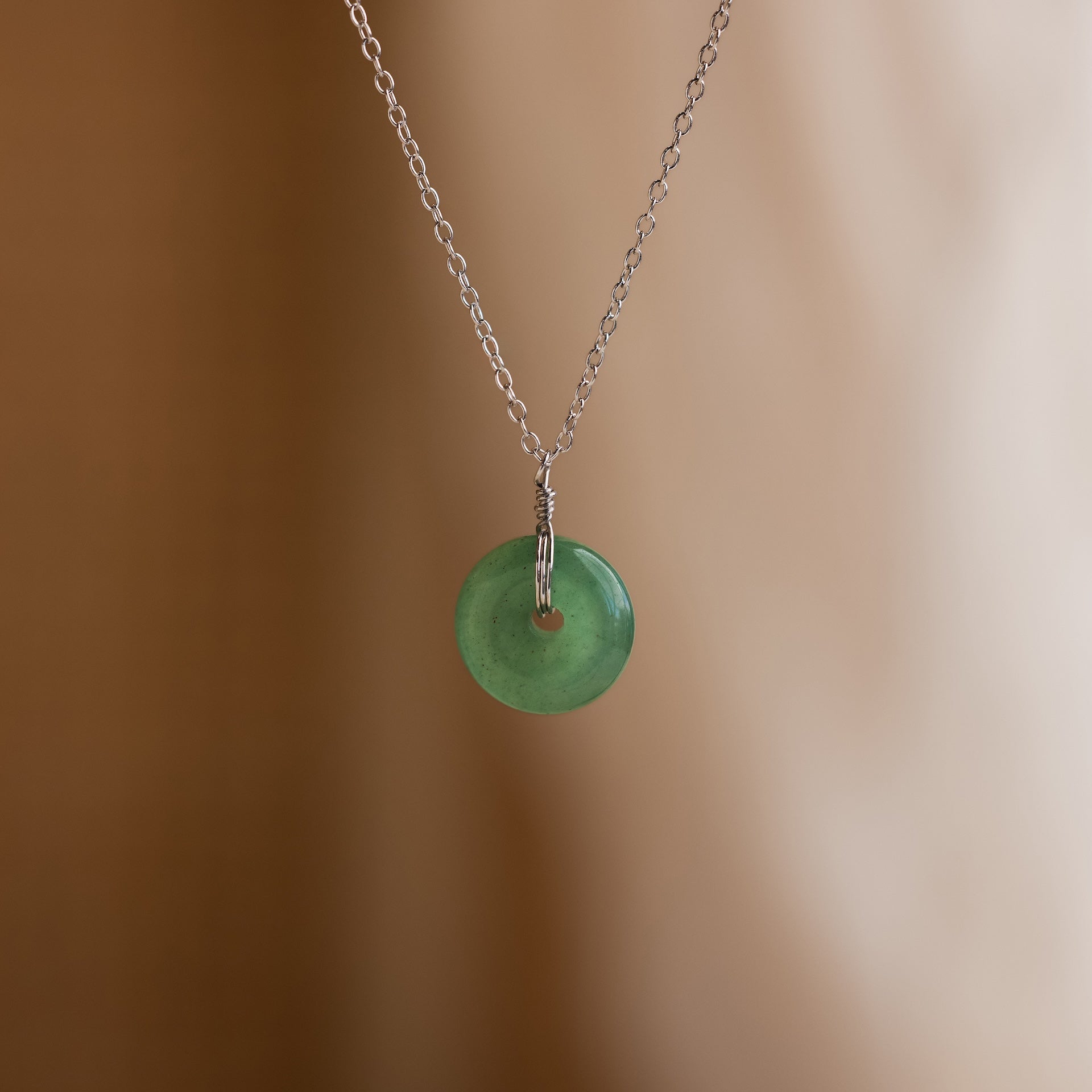 The Round Jade Pendant Necklace in Silver, featuring a jade gemstone, is showcased on a soft beige background, radiating natural elegance.