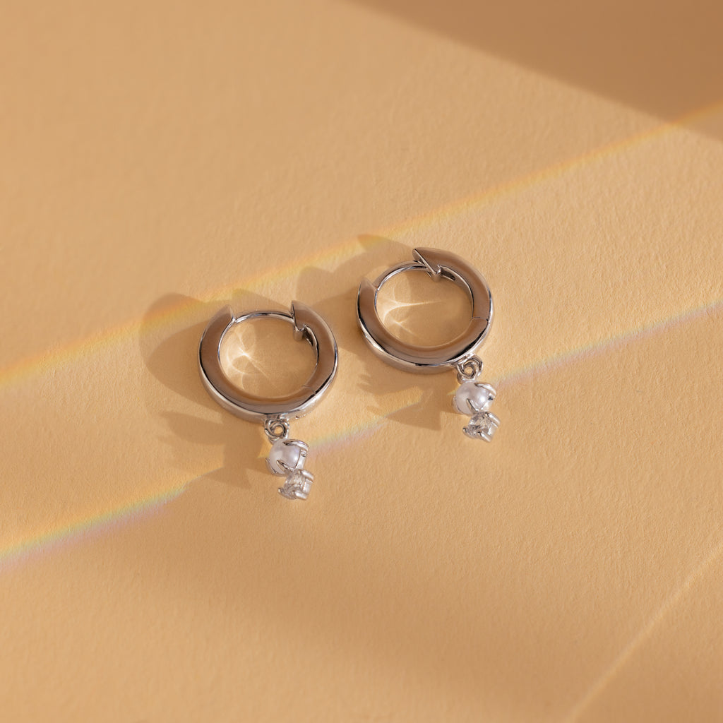 Dangling Pearl Diamond Huggies in Sterling Silver, these elegant earrings are showcased on a peach-colored background.