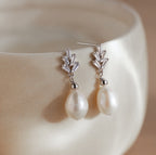 Pearl Diamond Drop Earrings in Silver featuring geometric tops and dangling white pearls, displayed on the rim of a cream-colored bowl.
