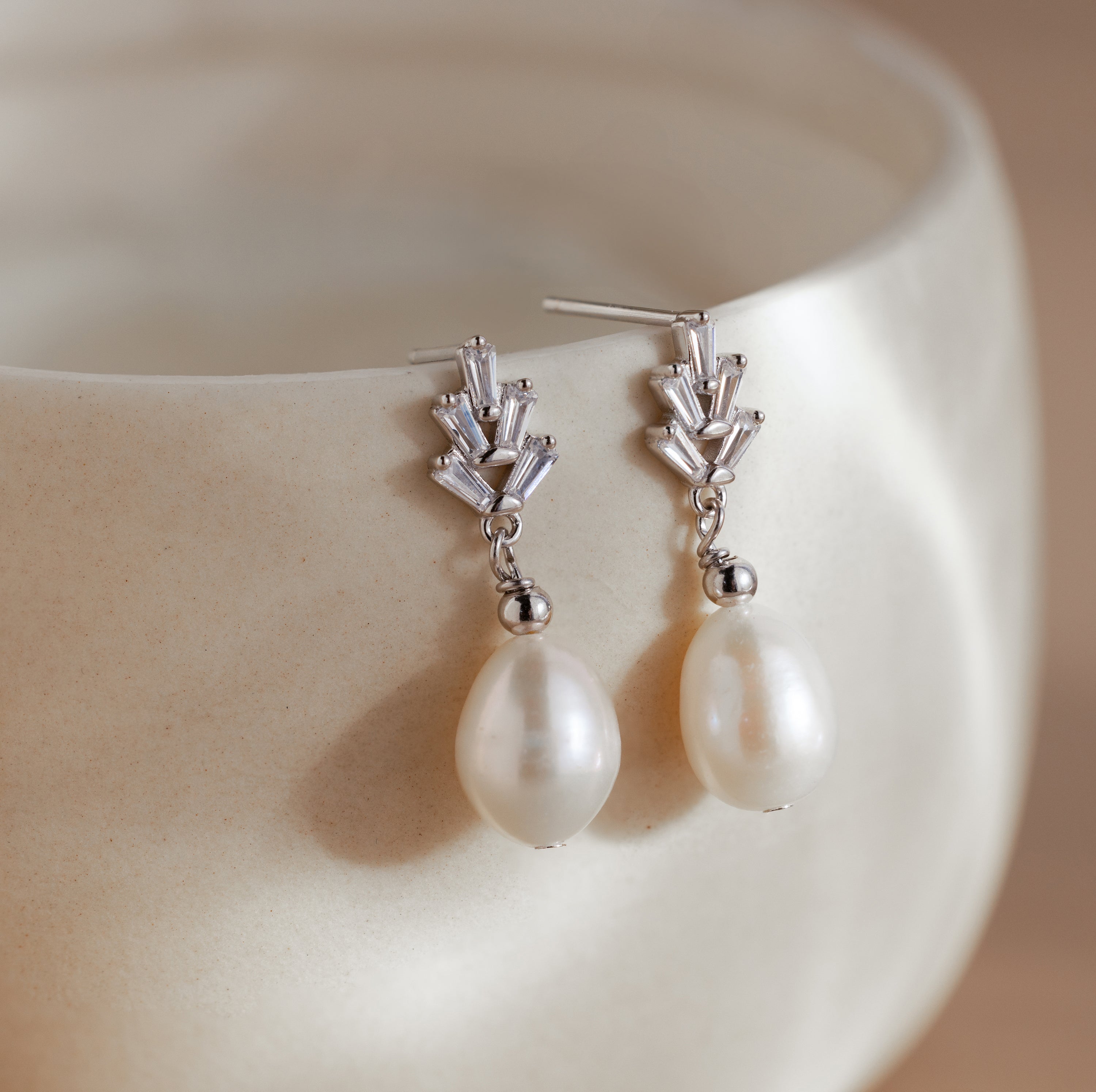 Pearl Diamond Drop Earrings in Silver featuring geometric tops and dangling white pearls, displayed on the rim of a cream-colored bowl.
