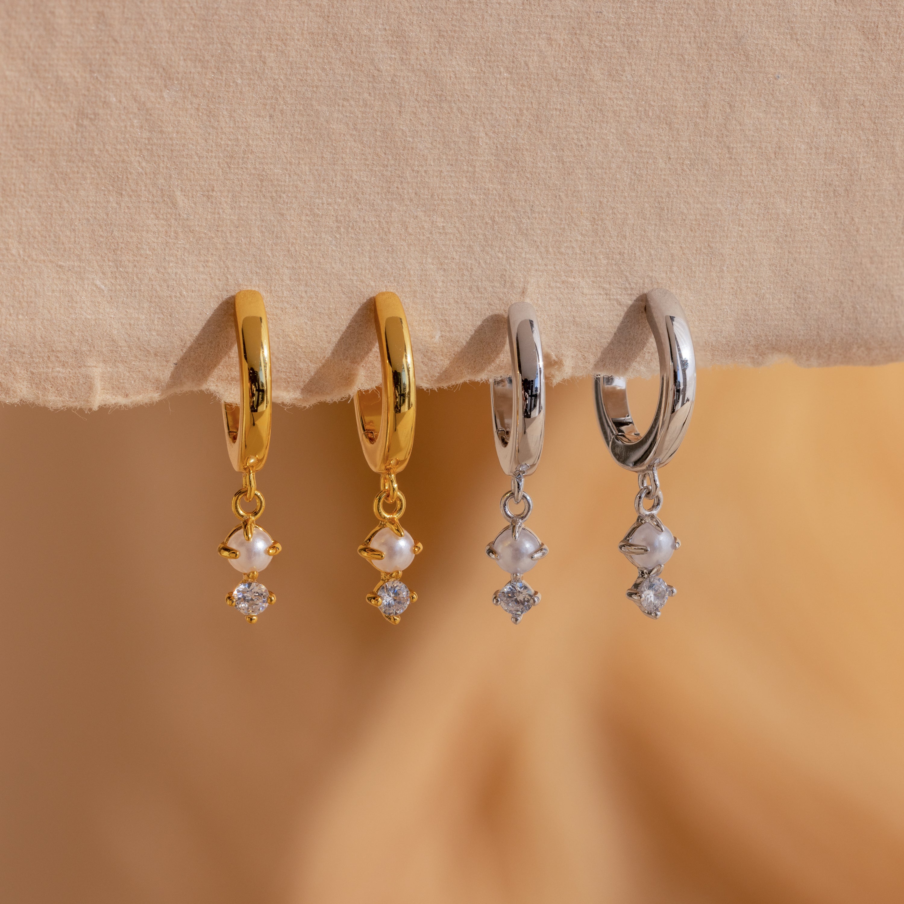 Two pairs of Dangling Pearl Diamond Huggies in 18K Gold, featuring gold and silver finishes with pearl and diamond-like charms, offer timeless elegance.