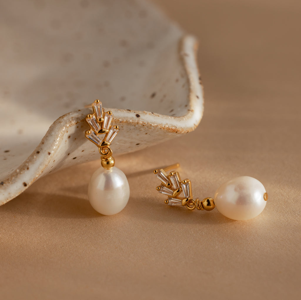 Pearl Diamond Drop Earrings in 18K Gold with crystal accents, vintage-inspired and elegant, are displayed on a beige surface next to a ceramic dish.