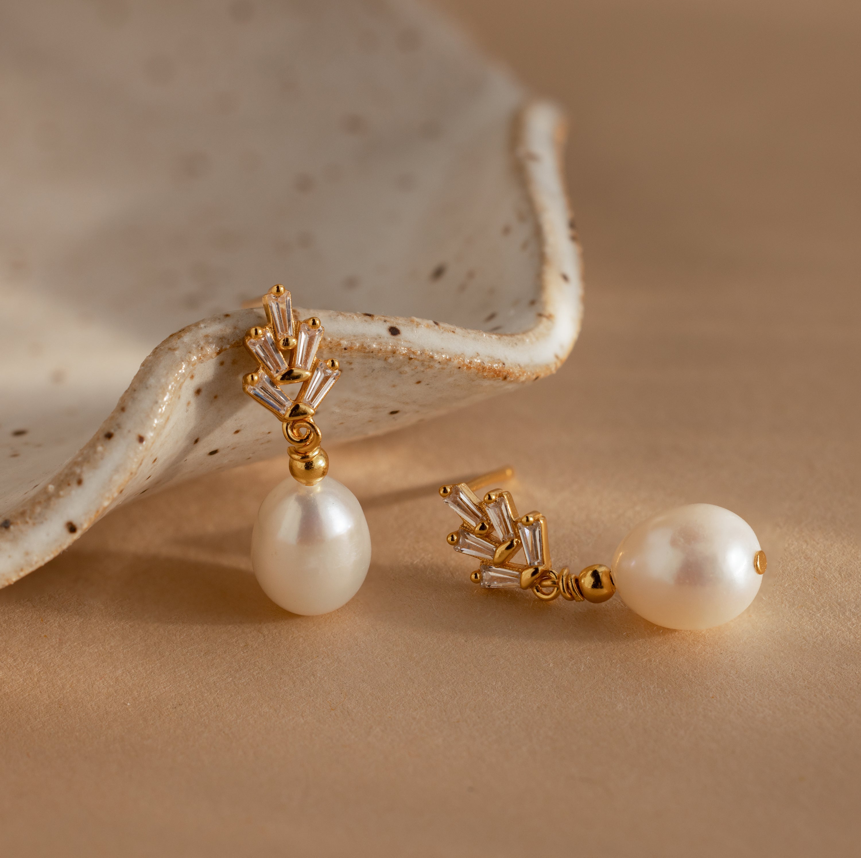 Pearl Diamond Drop Earrings in 18K Gold with crystal accents, vintage-inspired and elegant, are displayed on a beige surface next to a ceramic dish.