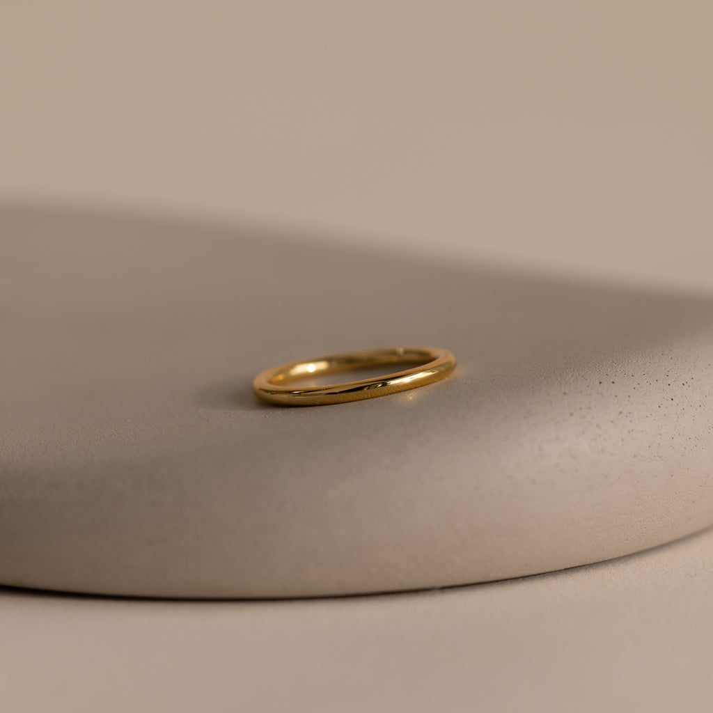 The Minimal Stacking Ring in 18K Gold is displayed on a smooth, beige stone surface with a neutral background—perfect for adding to your finger stack.