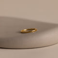 The Minimal Stacking Ring in 18K Gold is displayed on a smooth, beige stone surface with a neutral background—perfect for adding to your finger stack.