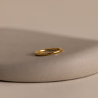 The Minimal Stacking Ring in 18K Gold is displayed on a smooth, beige stone surface with a neutral background—perfect for adding to your finger stack.