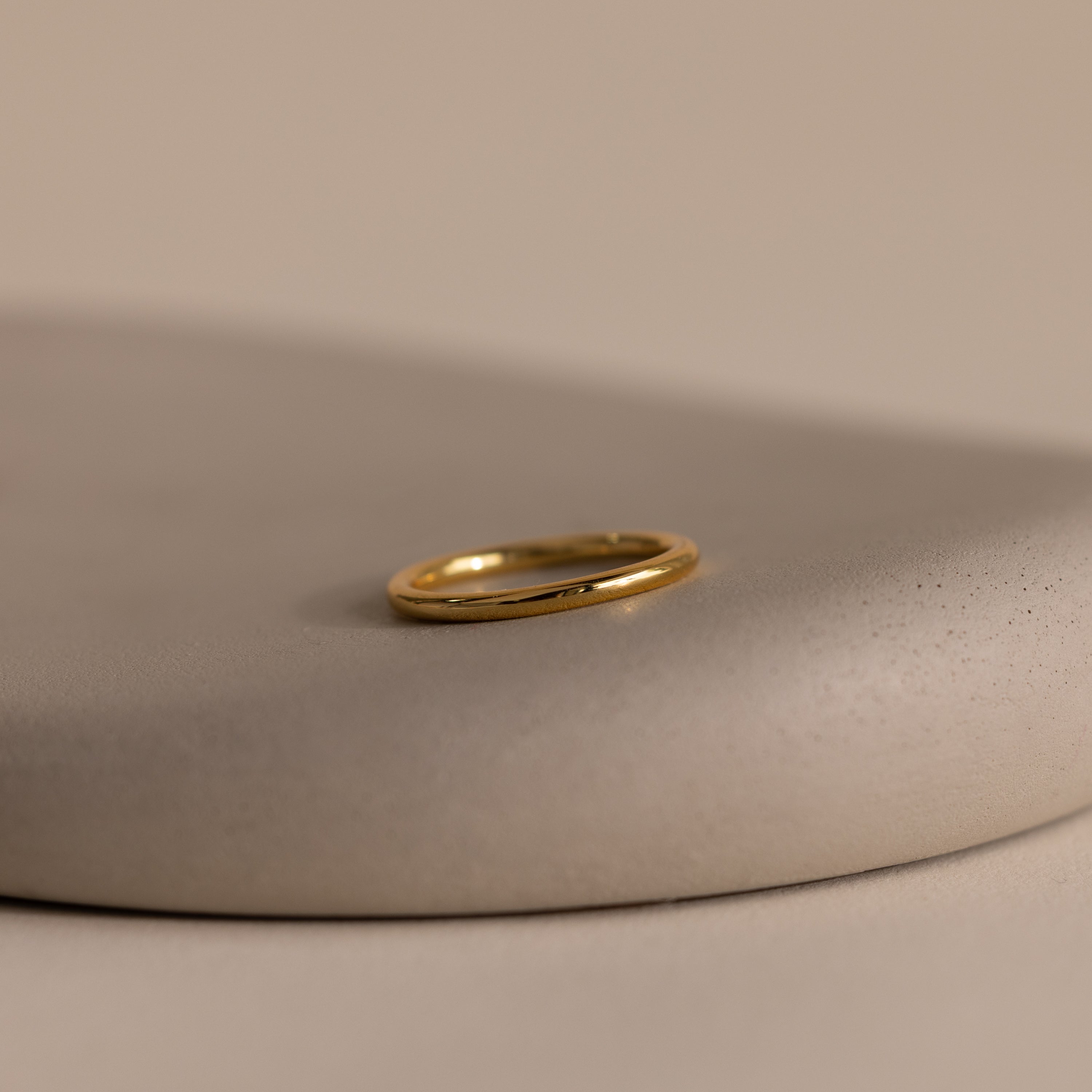 The Minimal Stacking Ring in 18K Gold is displayed on a smooth, beige stone surface with a neutral background—perfect for adding to your finger stack.