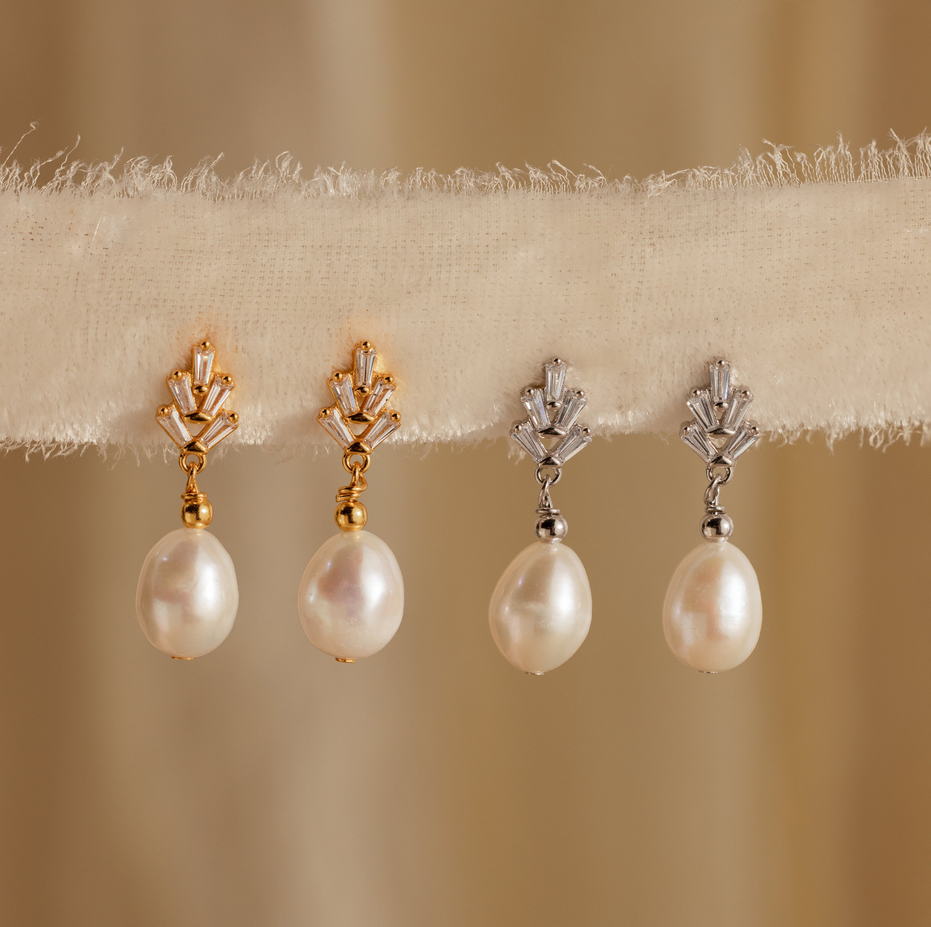 Two pairs of Pearl Diamond Drop Earrings in 18K Gold are displayed on a textured beige fabric.