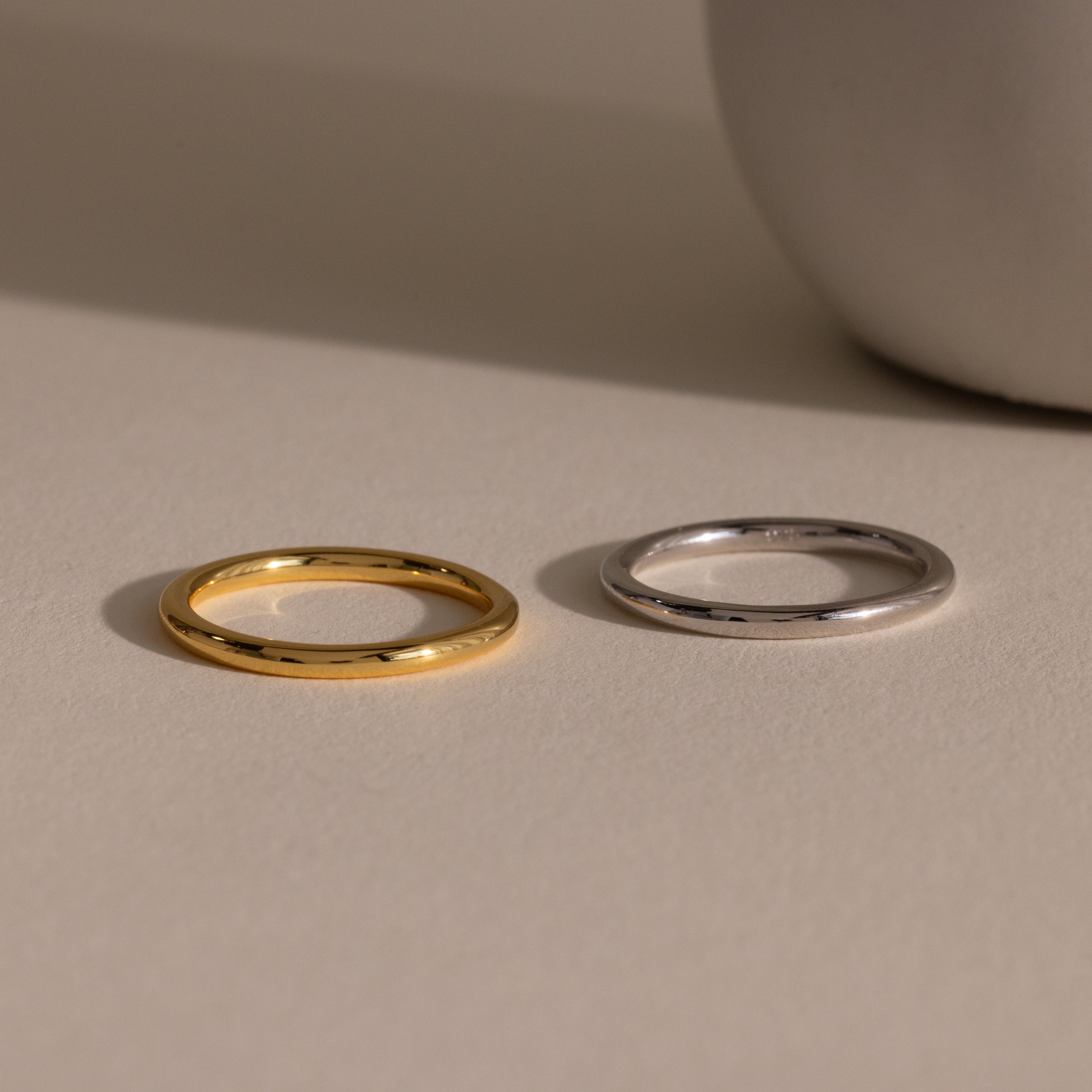 A Minimal Stacking Ring in Silver rests on a beige surface near a round white object.