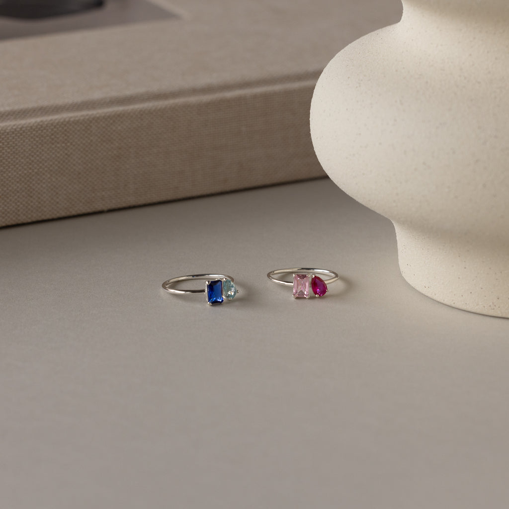 The Toi et Moi Birthstone Ring in Sterling Silver features vibrant blue and pink gemstones—customizable and perfect as a thoughtful Christmas gift, beautifully displayed on a neutral surface.
