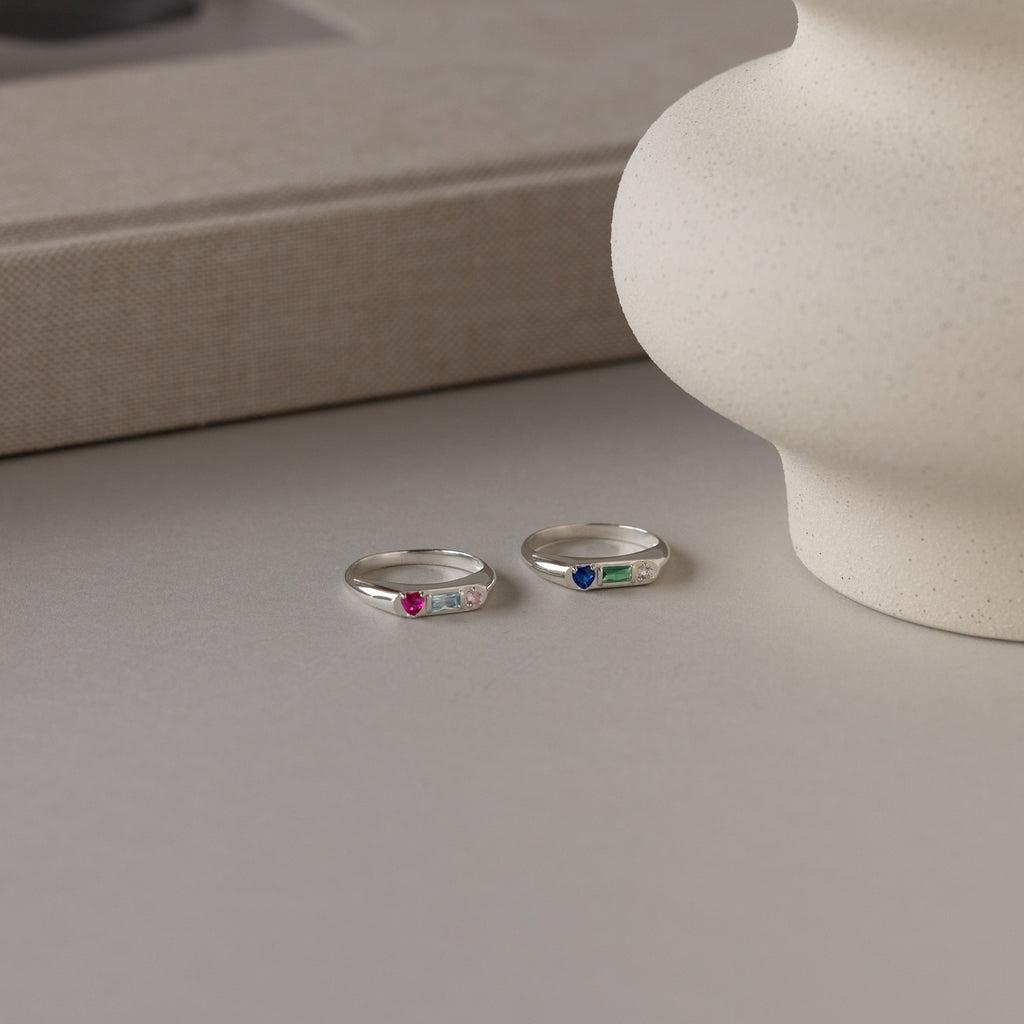 The Bold Birthstone Signet Ring in Sterling Silver features a colorful gemstone and rests on a neutral surface near a textured ceramic vase—perfect for those seeking customizable jewelry.