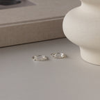 Two sterling silver rings with elegant cursive rest on a light surface by a textured vase and beige book—ideal as personalized rings like the Grace Script Name Ring in Sterling Silver, crafted in an exquisite script font.