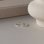 Two Ann Thin Message Rings in sterling silver with custom engraving rest on a smooth surface beside a beige vase and textured box—perfect as a thoughtful holiday gift.