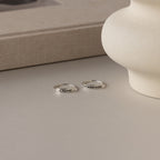 Two sterling silver rings on a beige surface; one is a skinny band engraved with "Oliver," while the other is the Flower Bar Ring in Sterling Silver with small decorative botanical jewelry symbols.