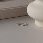 A Paris Thin Name Signet Ring in Sterling Silver, custom-engraved with the names Anna and Josh, rests on a neutral-colored surface beside a round vase.