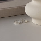 Two Newsletter Curb Name Rings in Sterling Silver, engraved with HOPE and PEACE, rest on a neutral tabletop beside a beige vase, highlighting their elegant curb chain-inspired design.