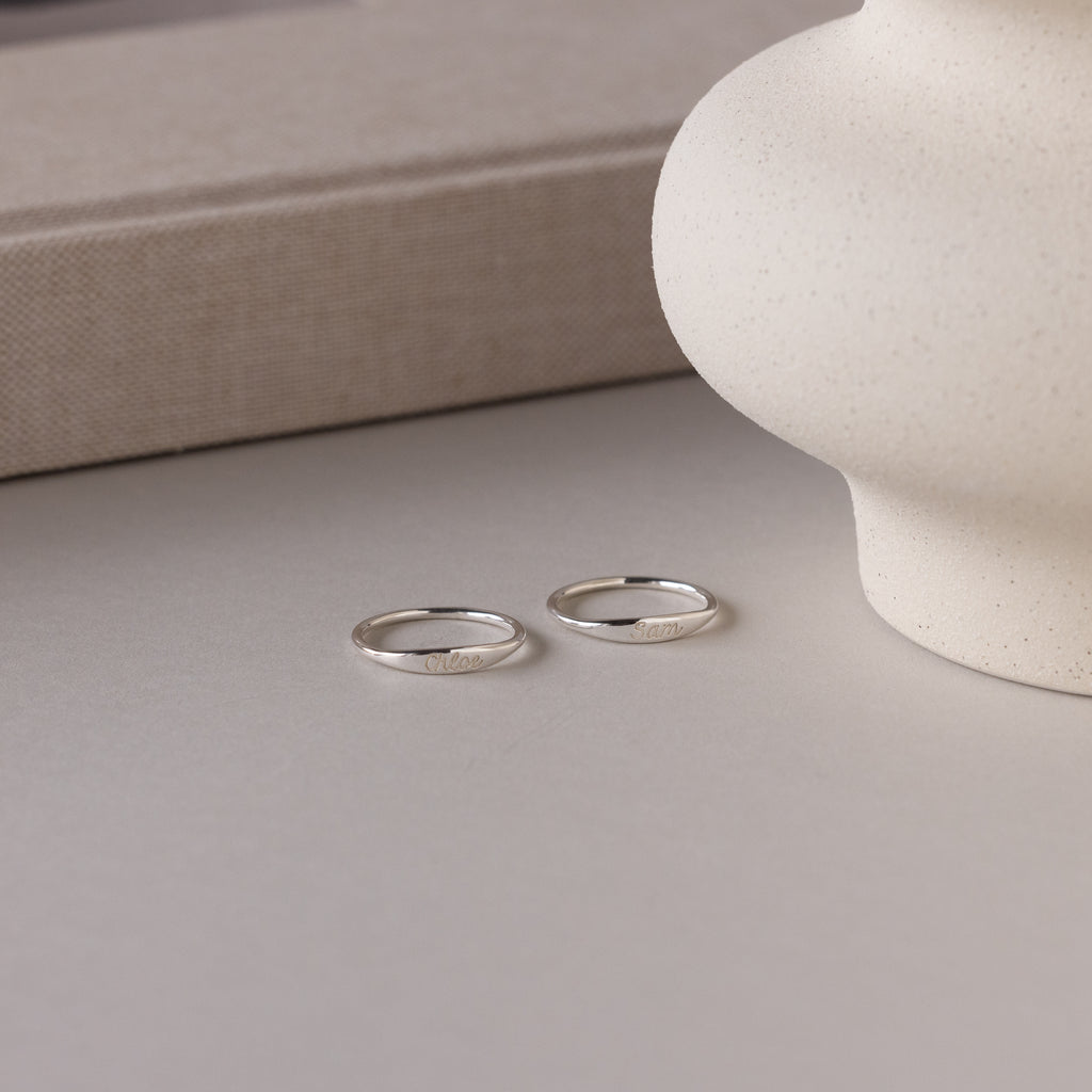 The Ann Skinny Name Ring in Sterling Silver rests on a light surface beside a textured vase and beige book—an elegant Christmas gift for her.