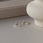 Two Roman Numerals Rings in Sterling Silver rest on a light surface beside a white ceramic vase and a beige book—an elegant milestone gift.