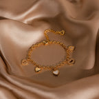 The Heart Charm Bracelet in 18K Gold, displayed on smooth champagne satin, features delicate heart charms—an elegant gift for your girlfriend.