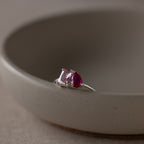 The Toi et Moi Birthstone Ring in Sterling Silver, with one pink and one red gemstone, sits on the edge of a round ceramic bowl.