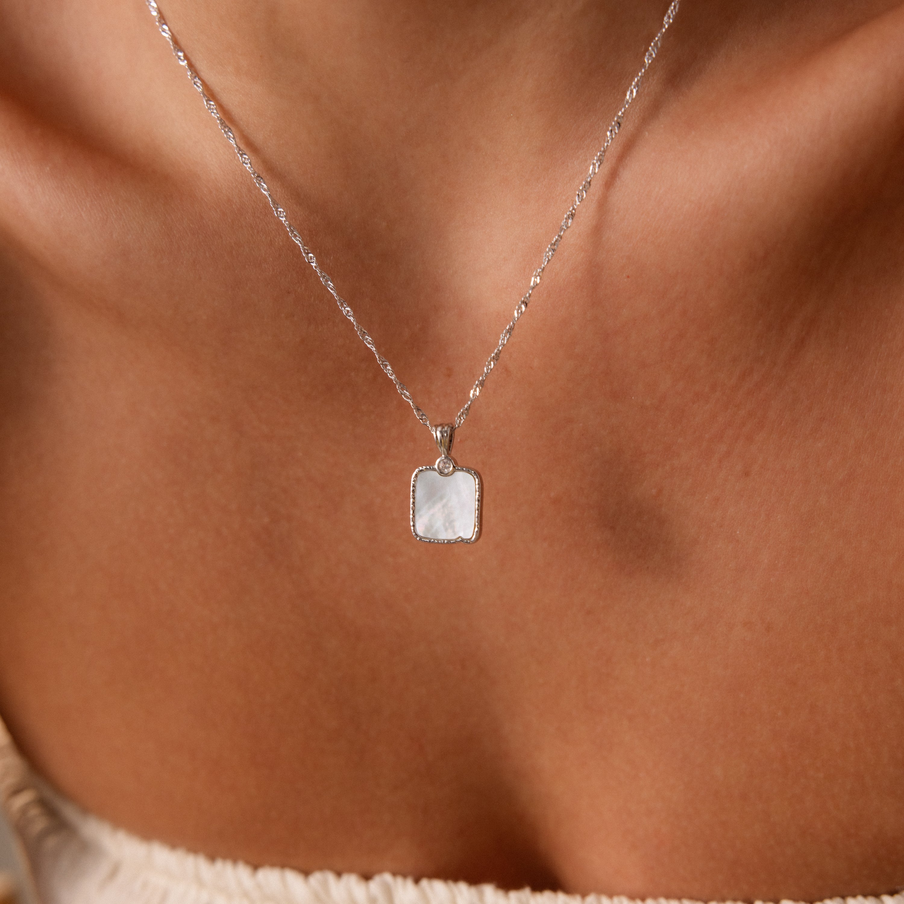 The Square Mother of Pearl Necklace features an iridescent, delicate pendant elegantly worn around the neck.