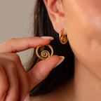 A woman holds a Spiral Swirl Hoop in 18K Gold near her ear, where she wears its match—ideal boho vacation jewelry to elevate any outfit.