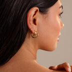 A woman’s ear with Spiral Swirl Hoops in 18K Gold, pearl studs, and a gold cuff—perfect boho vacation jewelry for a beachy vibe.