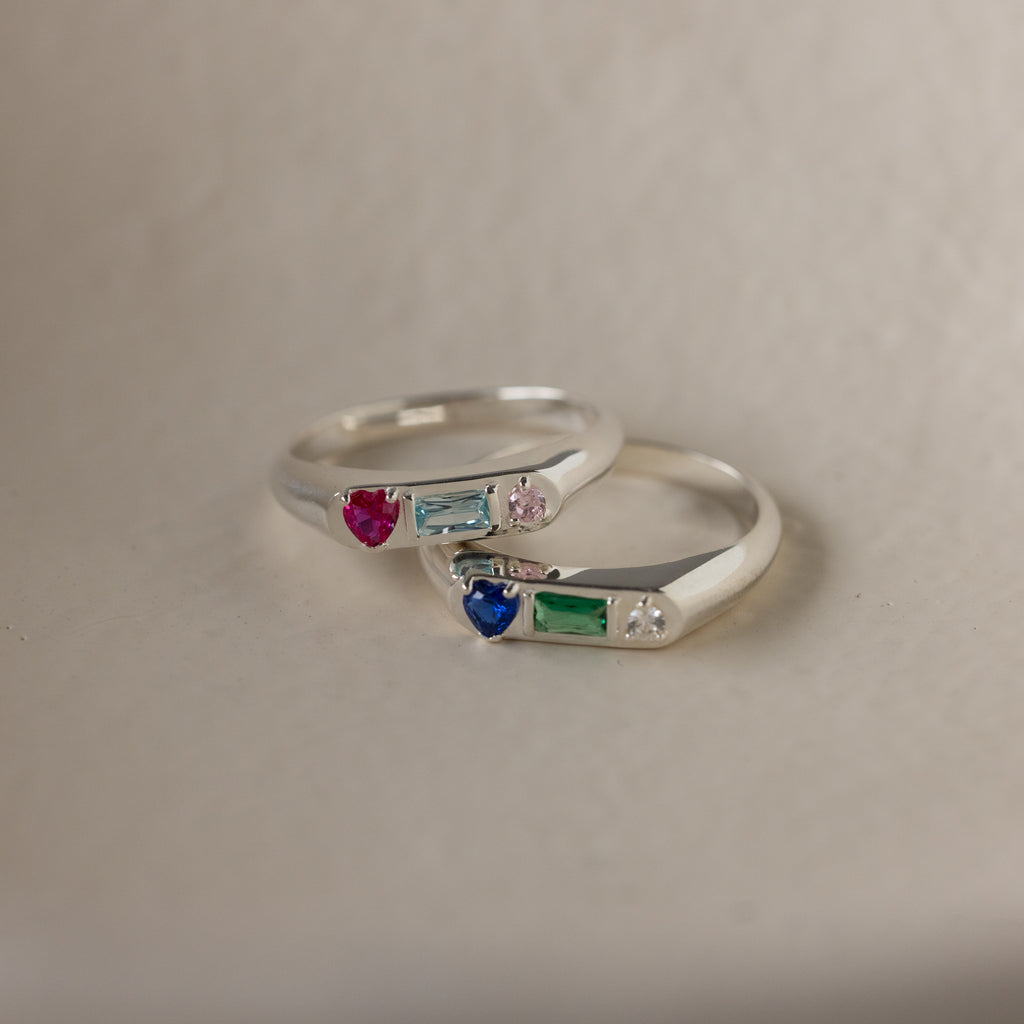 The Bold Birthstone Signet Ring in Sterling Silver features vibrant red, blue, green, and clear gemstones—beautifully set on a neutral background. A perfect customizable jewelry piece to celebrate and cherish special moments.