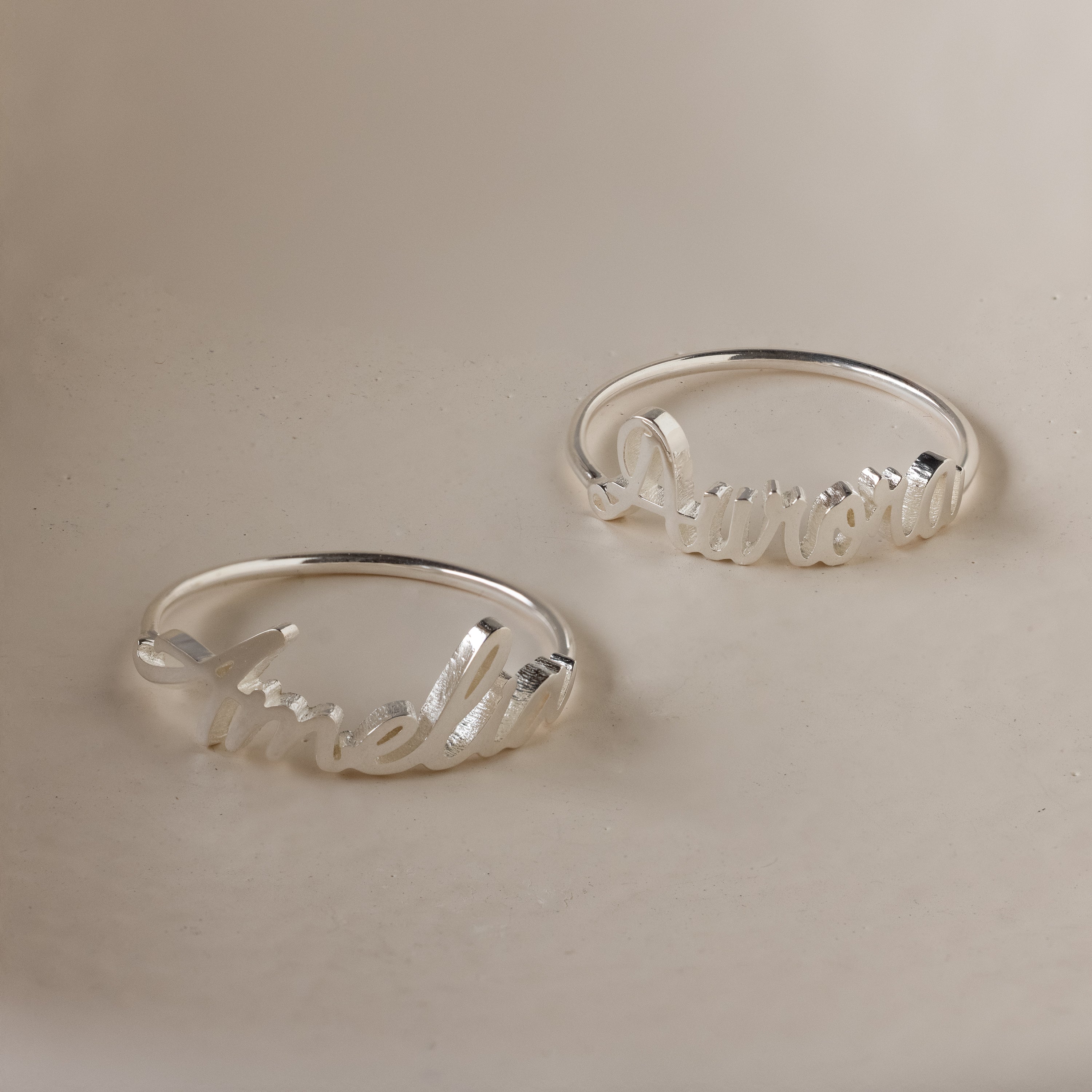 Two Grace Script Name Rings in Sterling Silver, each personalized with an elegant script font—one engraved with "Amelia," the other with "Aurora.
