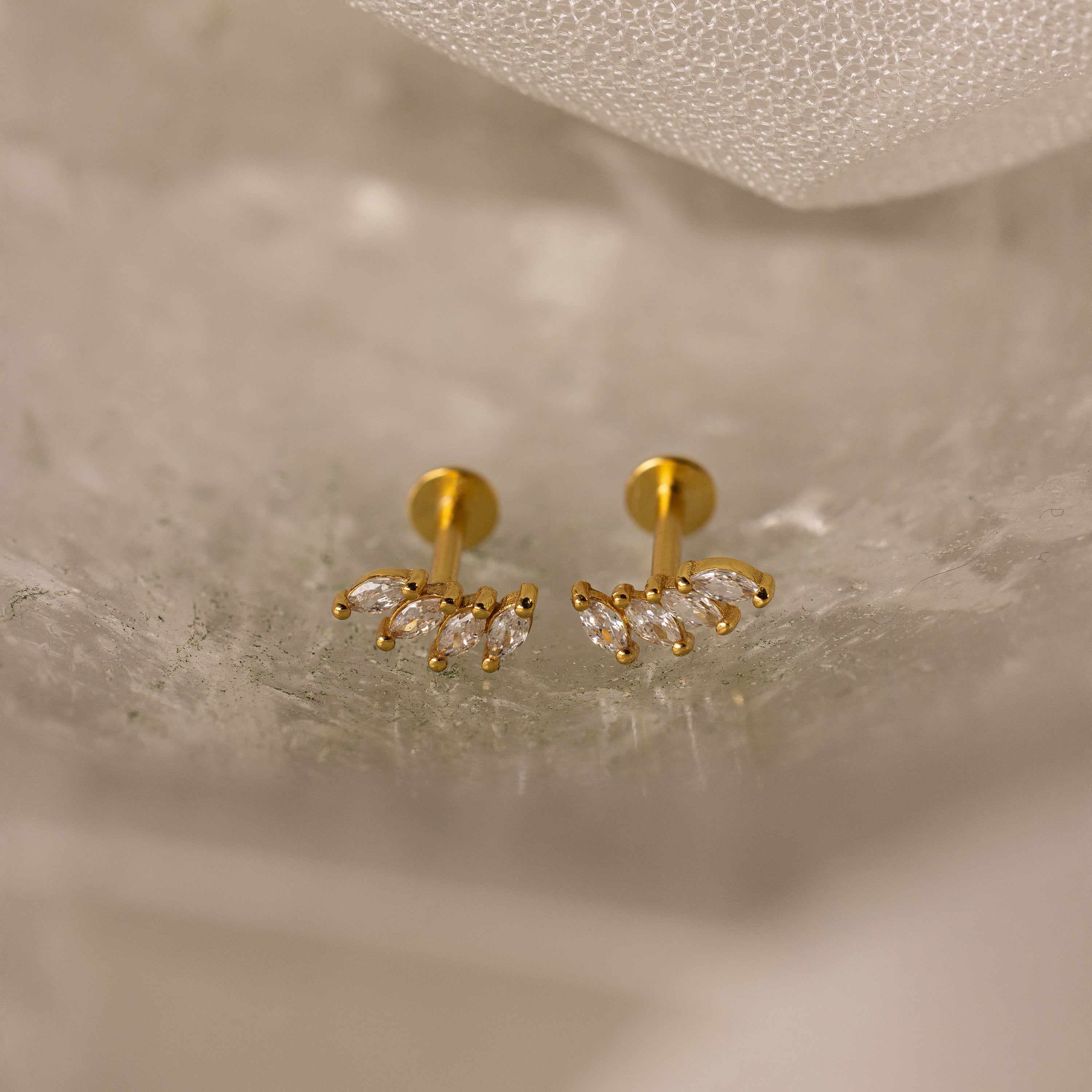 The Marquise Diamond Climbers in 18K Gold feature small, leaf-shaped clear stones—an elegant choice for wedding jewelry, shown on a light, textured surface.